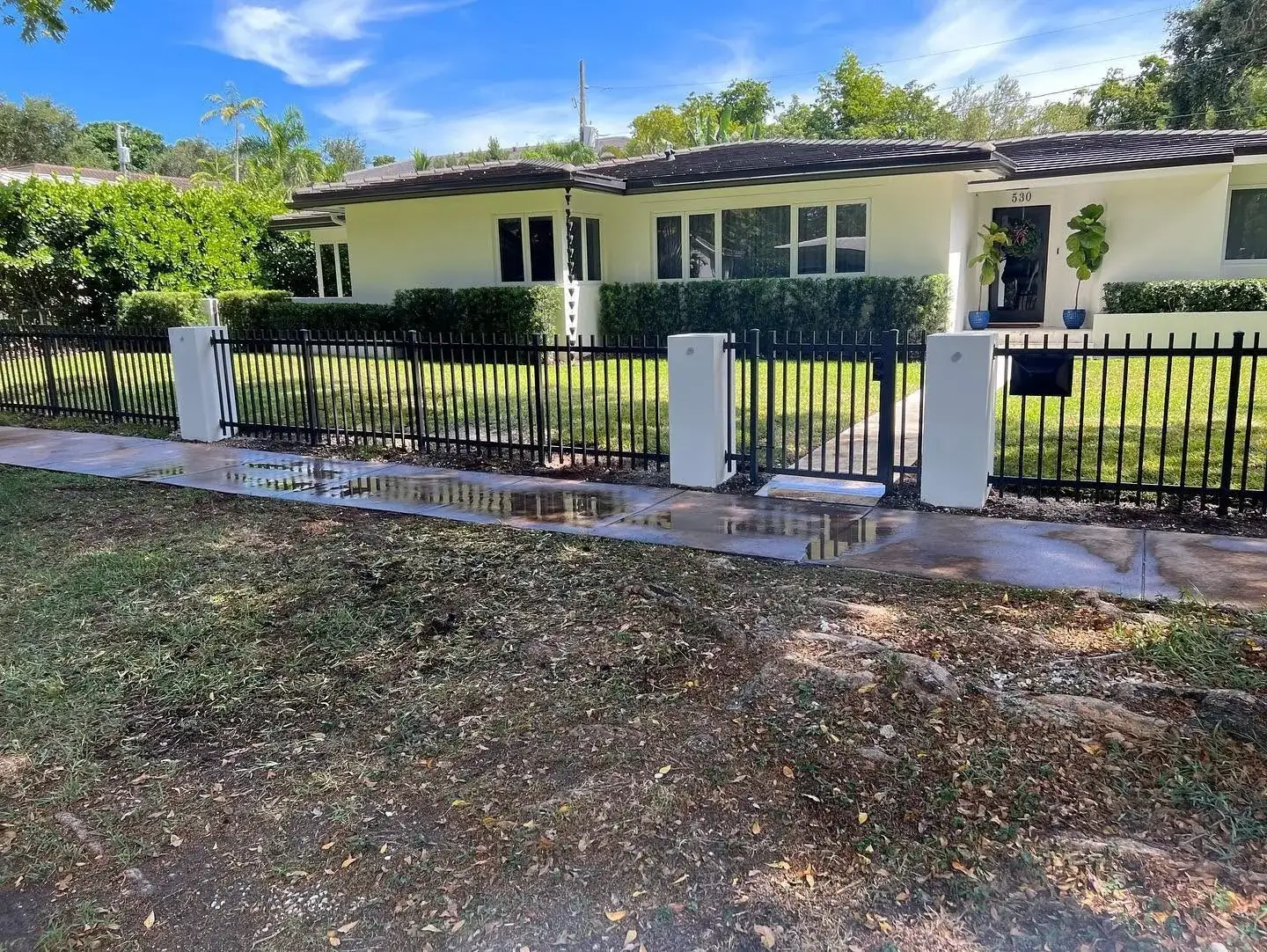 Black aluminum picket fence with stucco pillars framing a Miami driveway