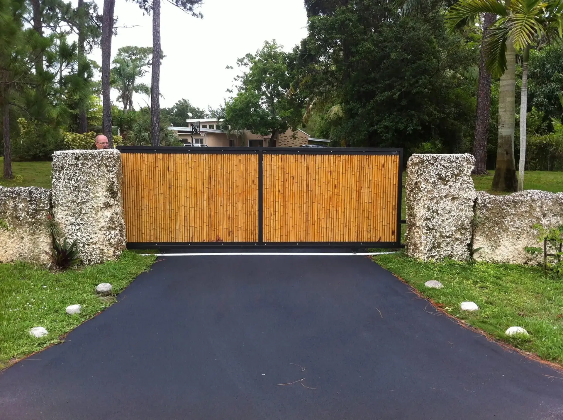 Custom wood driveway gate between coral rock pillars in Miami