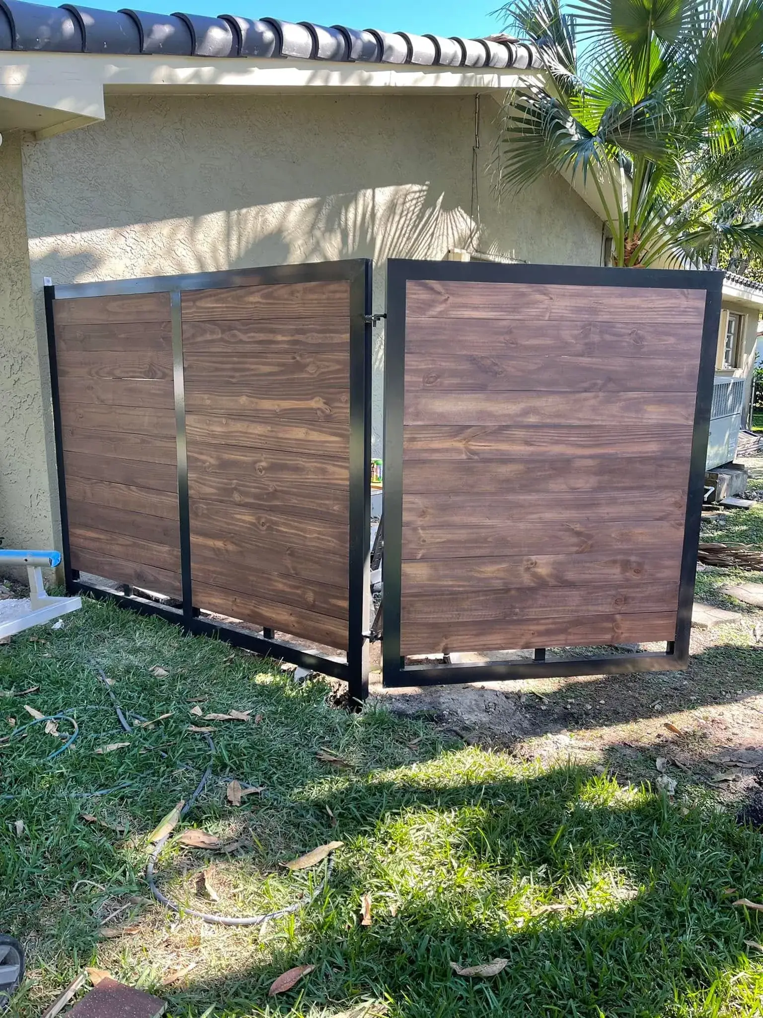 Dark wood driveway gate with black steel frame in Miami